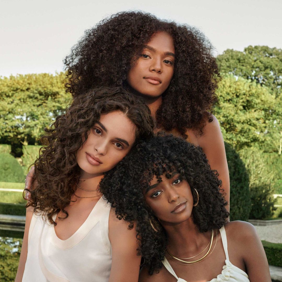 Three women wearing Aveda curly hair care products.