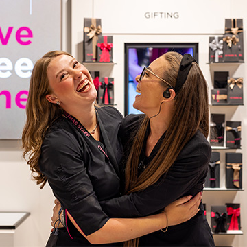 Deux collaborateurs d’ICI PARIS XL se prenant dans les bras dans le magasin, devant un présentoir de cadeaux et de produits de beauté.