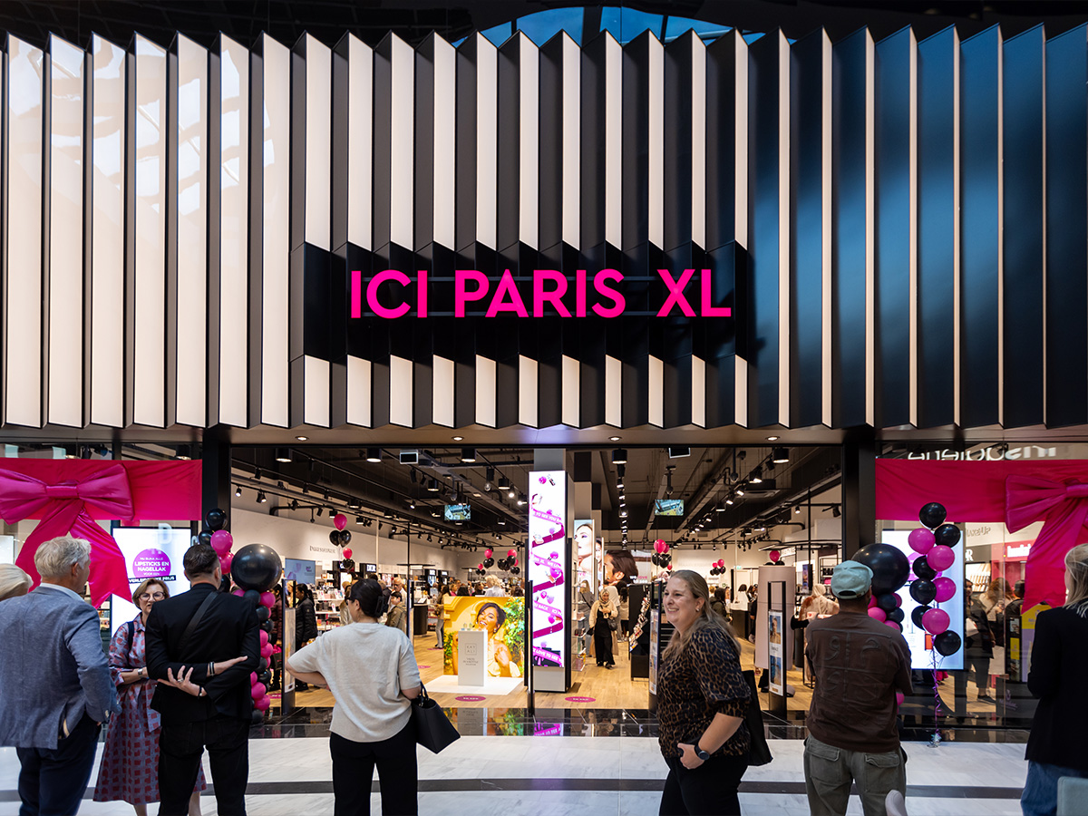 Façade d'un magasin ICI PARIS XL dans un centre commercial, décorée de nœuds et de ballons roses, avec des visiteurs rassemblés devant l'entrée.