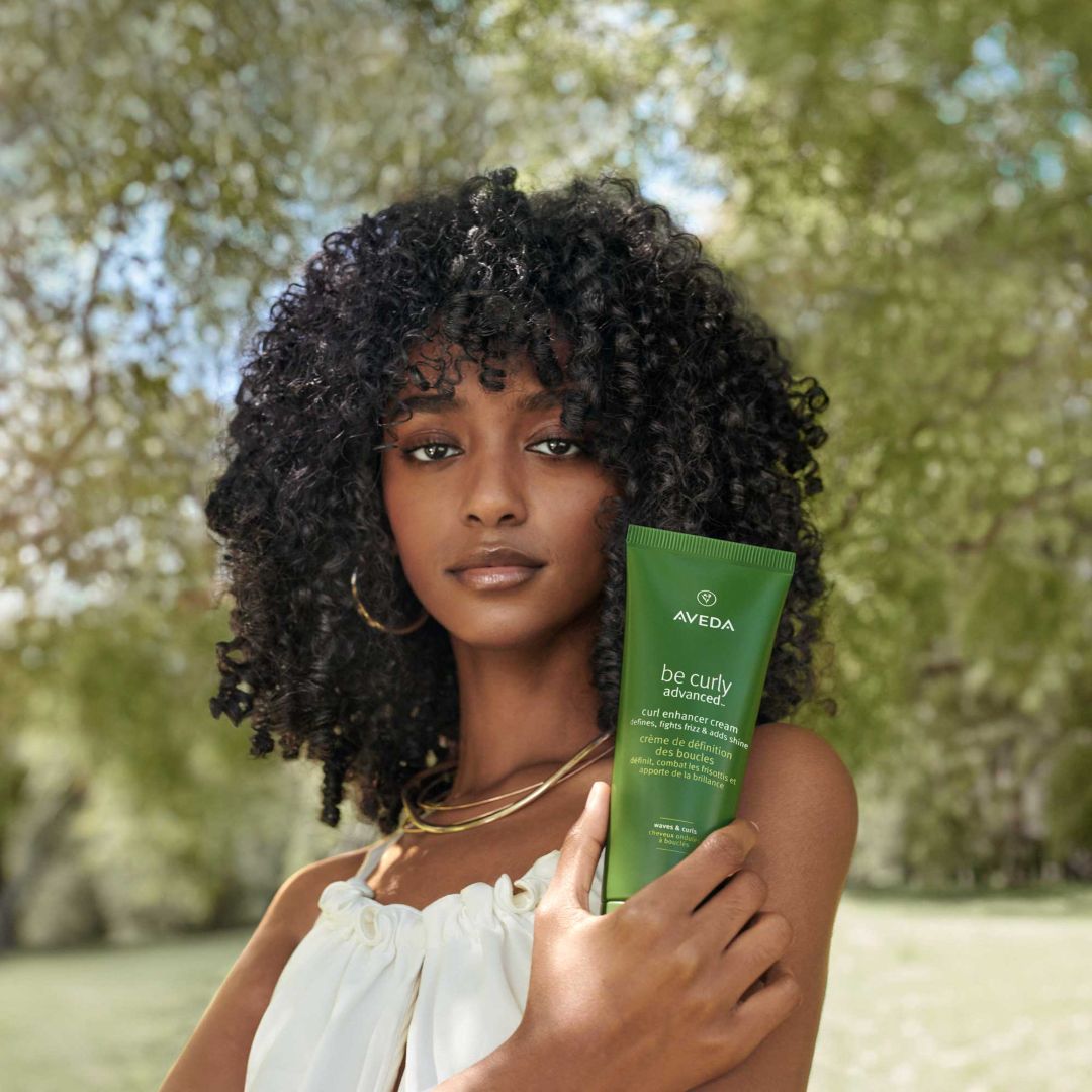 A woman holding Aveda curly hair care product.