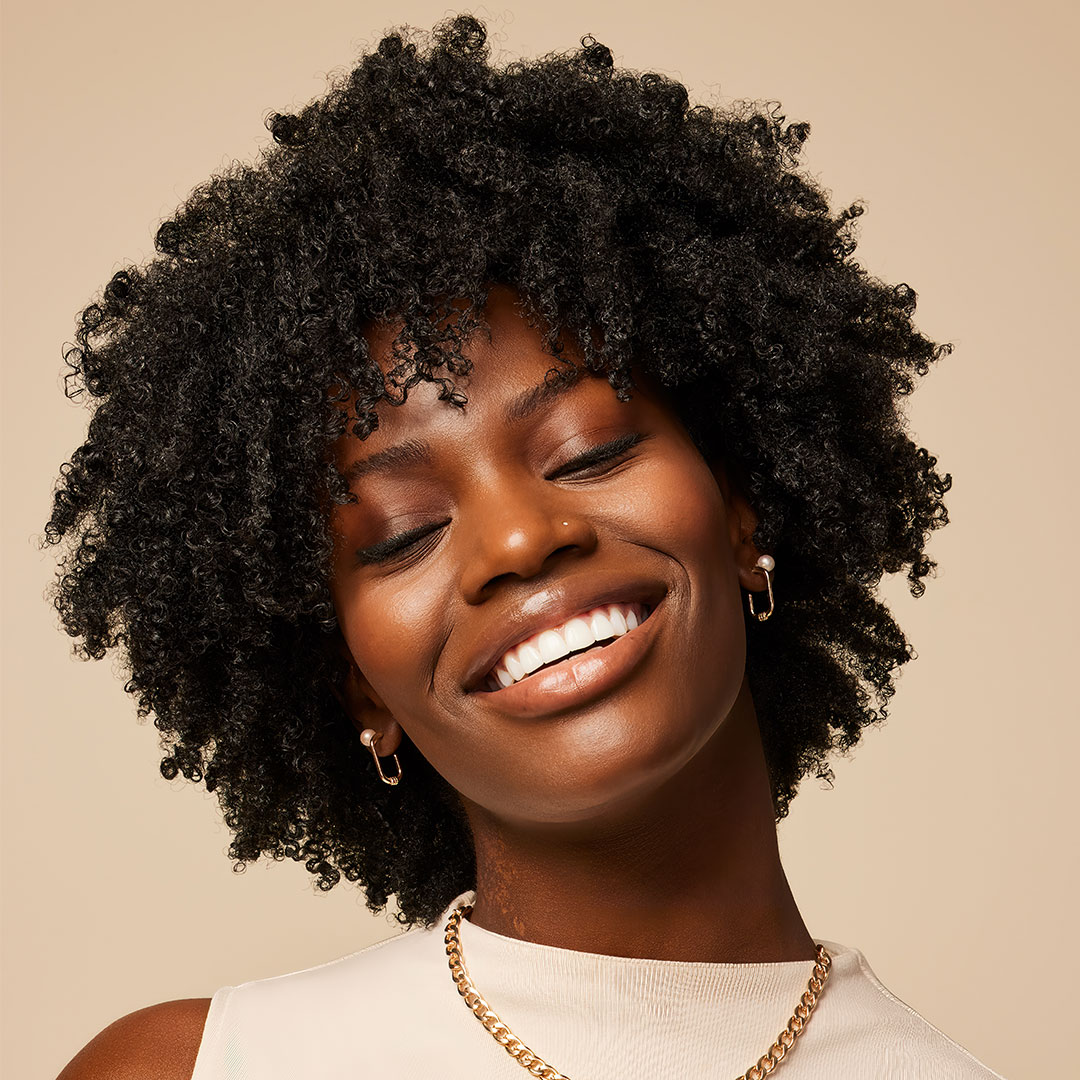 A woman holding Aveda curly hair care product.