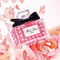 De flacon van het parfum Miss Dior Essence omringd door roze vlinders, bloemen en een Dior-lint