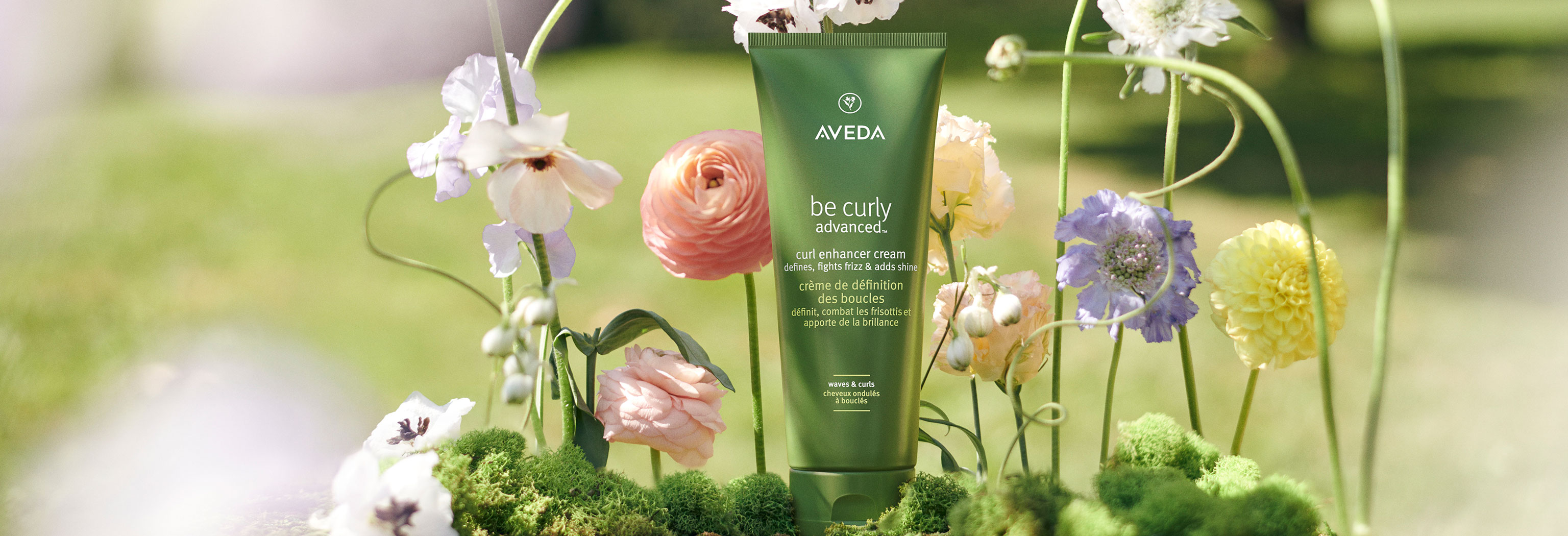 Hair care product by the brand Aveda surrounded by flowers in the background.
