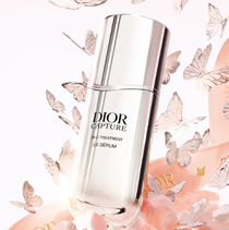De flacon van het serum Dior Capture, omringd door zilveren vlinders en bloemen en een roze Dior-lint
