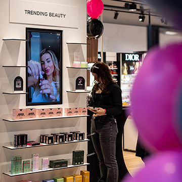 Client consultant des produits dans l’espace Trending Beauty d’un magasin ICI PARIS XL, avec un écran numérique et des produits de beauté présentés sur l’étagère.