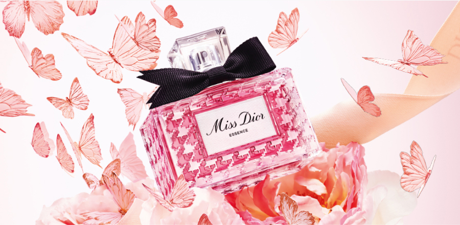 De flacon van het parfum Miss Dior Essence omringd door roze vlinders, bloemen en een Dior-lint