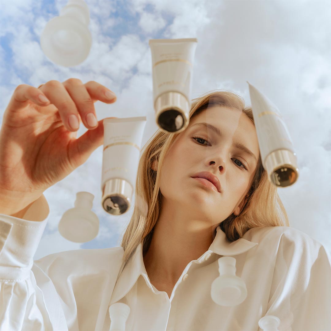 Femme tenant des tubes Phyto-Teint Primer Glow de Sisley sous un ciel nuageux