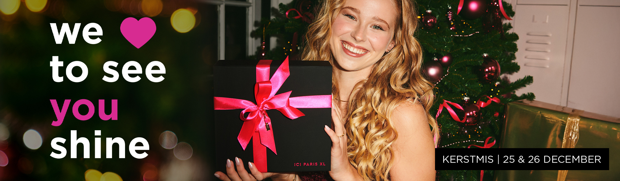 Vrolijke, lachende vrouw met cadeautje zittend voor een kerstboom.