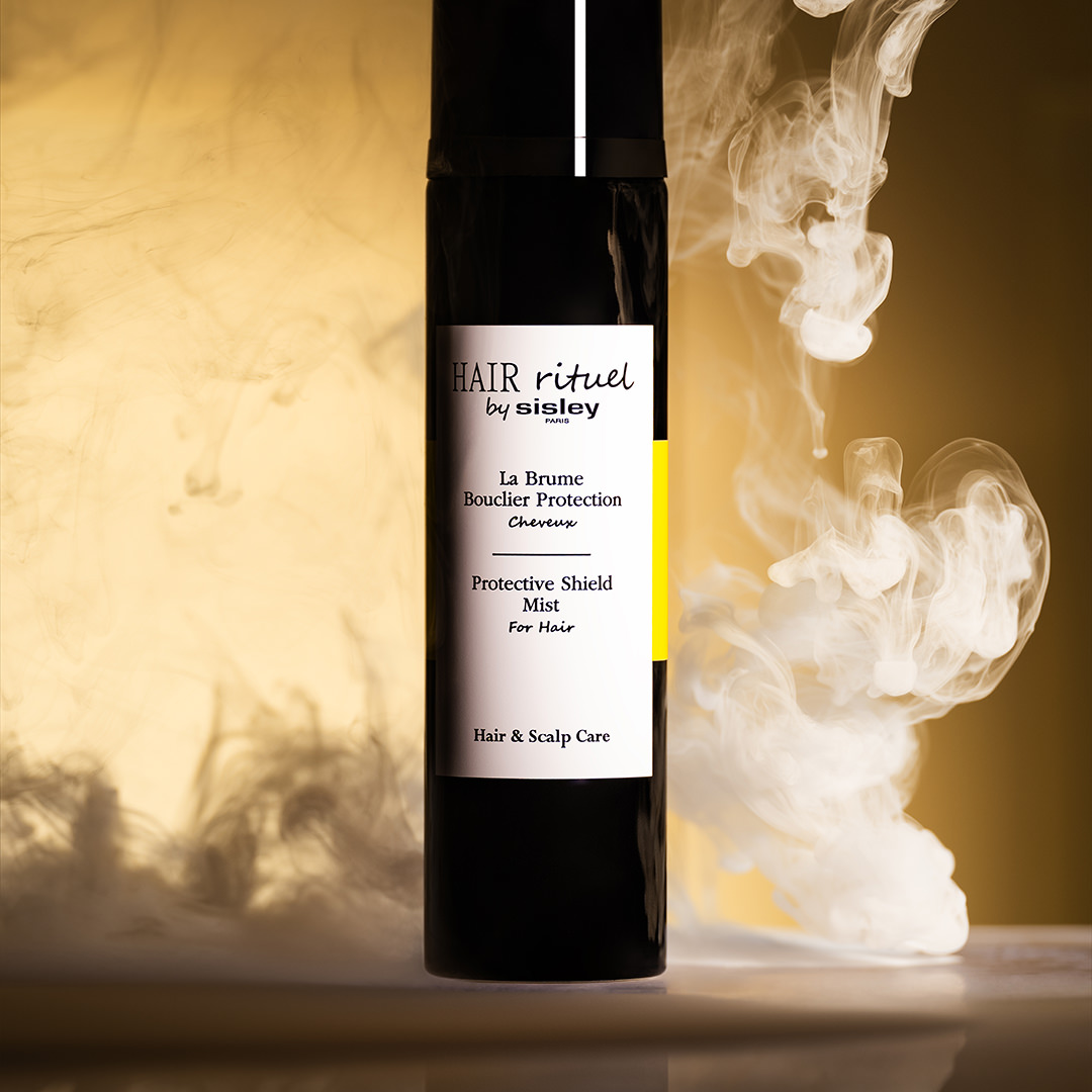 Hair Rituel by Sisley Protective Shield Mist standing amid swirling smoke on a golden background