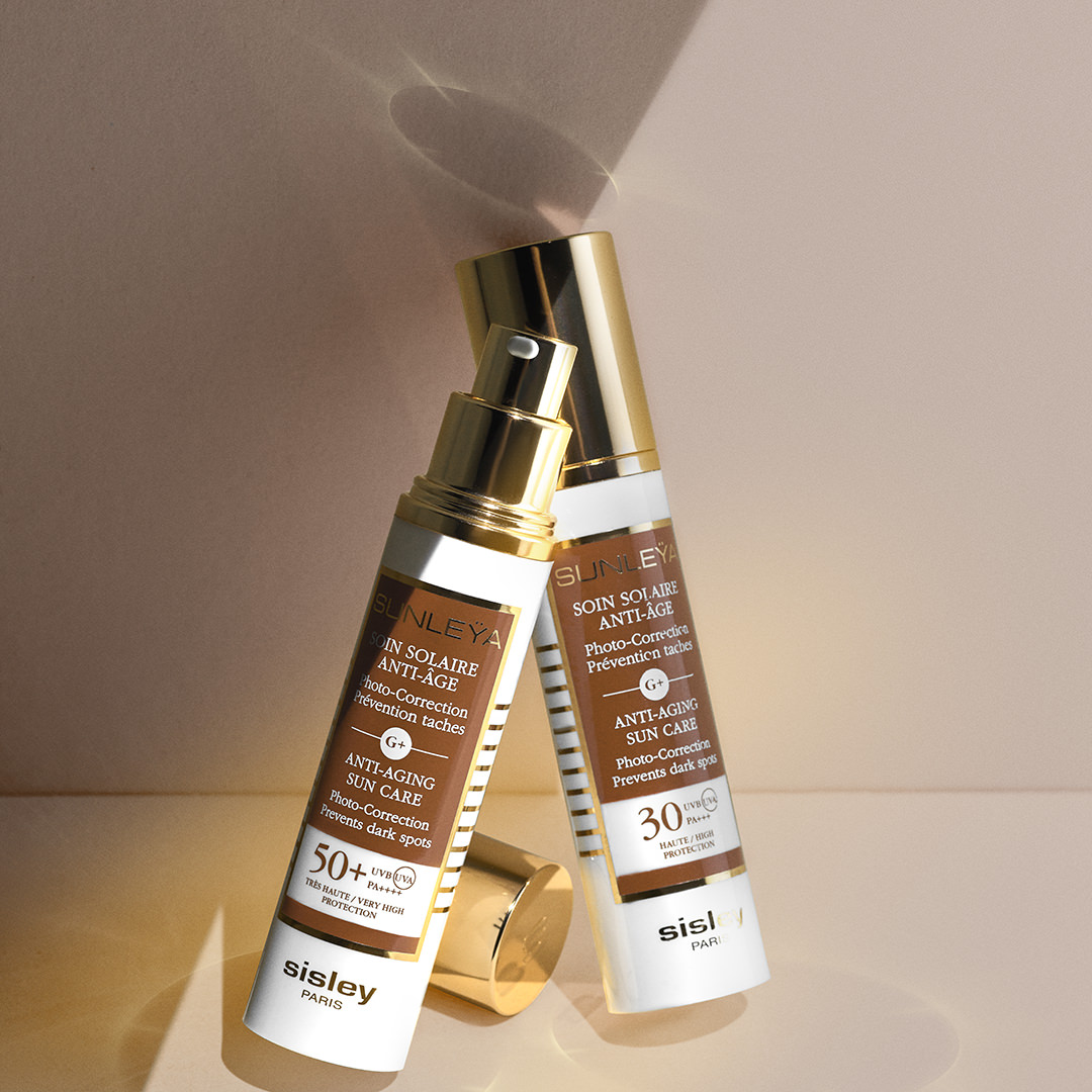Two Sisley Sunleÿa Anti-Aging Sun Care products with SPF 50+ and SPF 30 on a peach-toned background with soft shadows